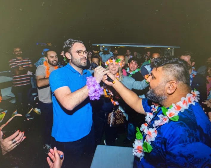 "Group of people enjoying music, food, and lights at a beachside party."