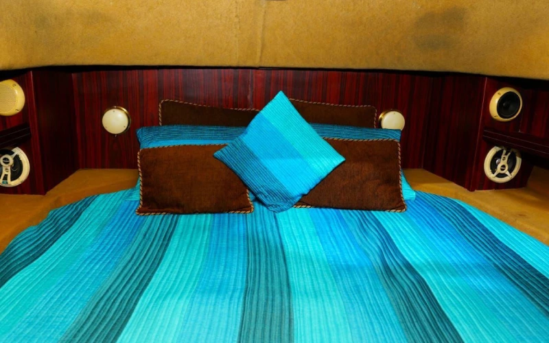 Cozy bedroom inside Blue Fin Yacht with soft bedding, side lamps, and sea-view window