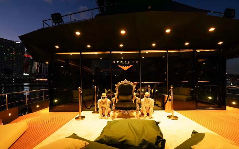 Luxurious outdoor deck of Stealth Yacht at night featuring a royal throne-style chair, ambient lighting, and golden statues for a majestic setting