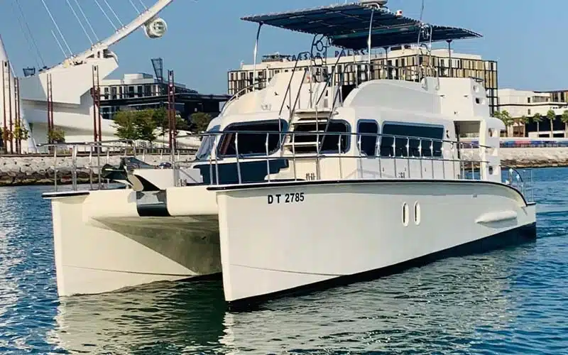 Side profile of luxurious catamaran anchored by Palm Jumeirah with panoramic glazing and spacious flybridge