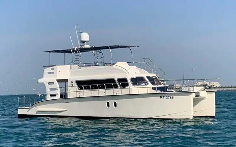 Spacious catamaran cruising along Dubai Marina waters with sleek twin‑hull silhouette and upper sun‑deck visible