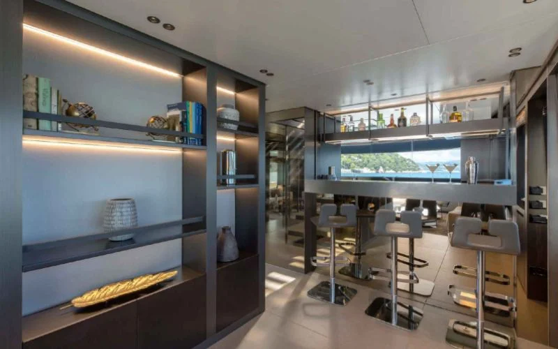 The modern and well-stocked bar on the Tiberias yacht by Malayachts.ae, featuring sleek bar stools, illuminated shelving, and a view of the ocean.