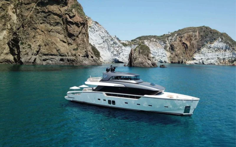 The luxury yacht Tiberias from Malayachts.ae cruising in a clear blue sea with dramatic rocky cliffs in the background.