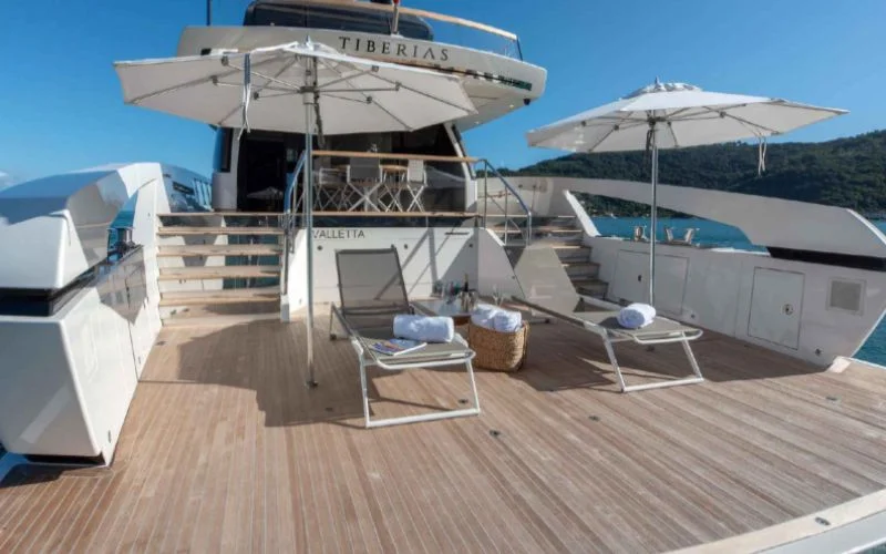 A view of the spacious deck of the luxury yacht Tiberias from Malayachts.ae, featuring sun loungers and umbrellas.