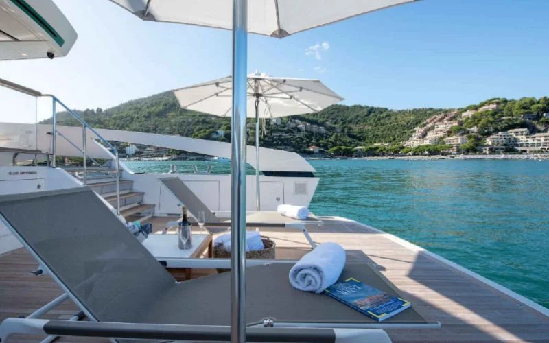 Relaxing on the spacious deck of the Tiberias yacht by Malayachts.ae, with sun loungers, towels, and a beautiful coastal backdrop.